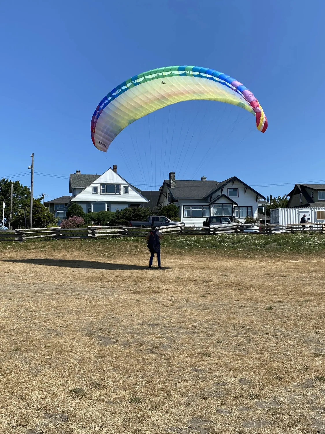 Colourful parafoil kite flying above a grassy open space
